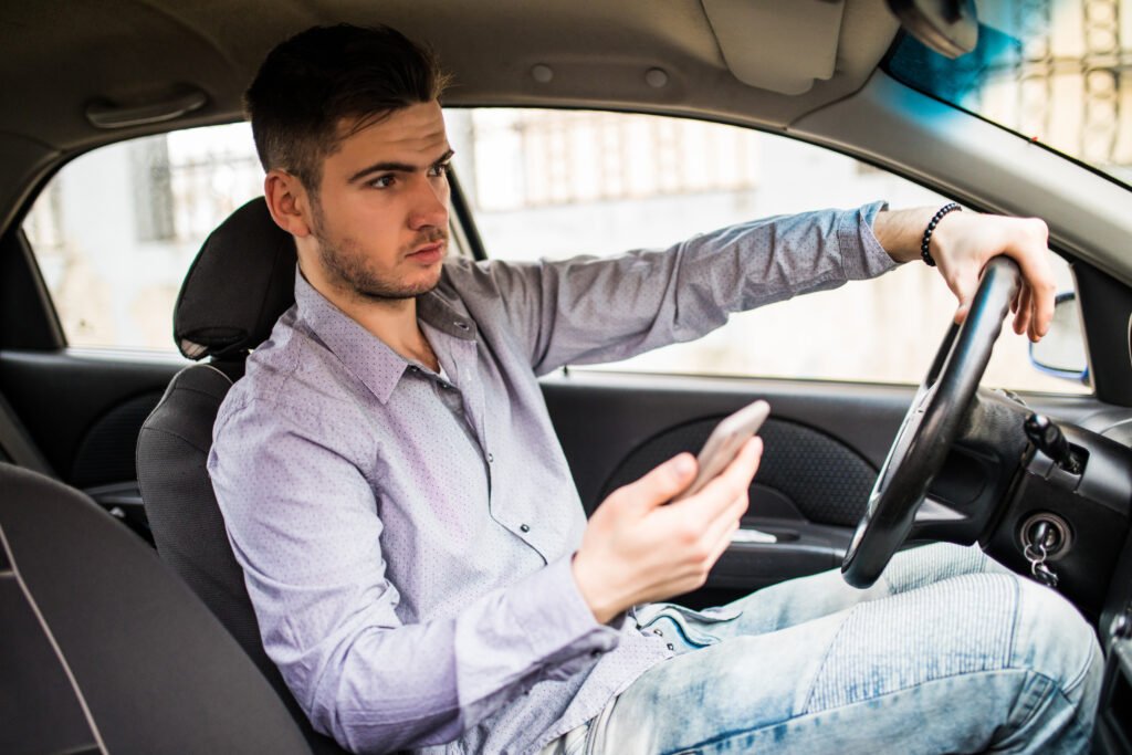 young man looking at mobile phone while driving a car.