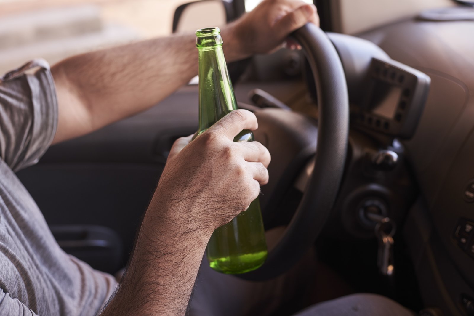 bottle of beer in a man's hands driving the car during daytime